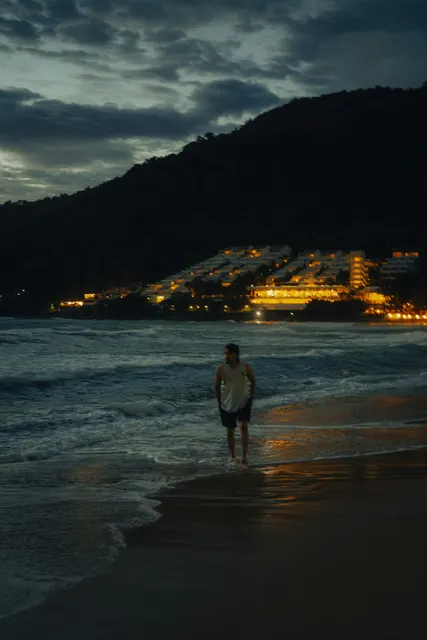 At blue hour, a lone figure walks through the surf on a dark beach beneath a clo